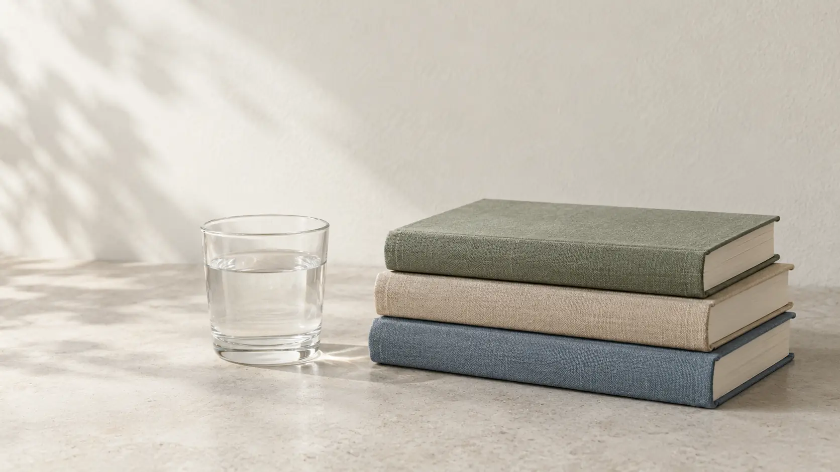 Three closed books and a glass of water on a concrete surface